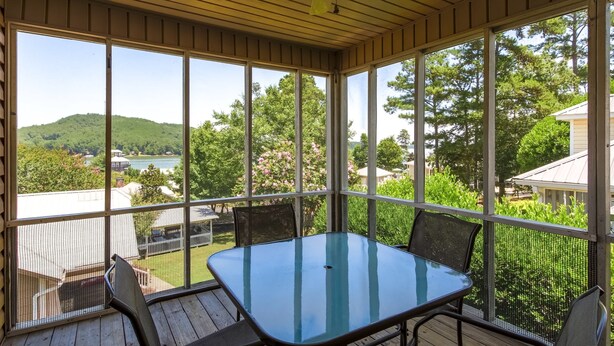 En overdækket terrasse med et bord og stole, store vinduer der giver udsigt over en sø og bakker.