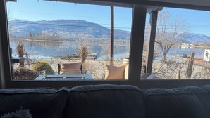 A room with a large window overlooking a lake and mountains, a couch, and a table with chairs. - Osoyoos Lakeview Villa Canada's Warmest Paradise (Osoyoos)