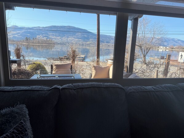 A room with a large window overlooking a lake and mountains, a couch, and a table with chairs.