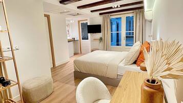Een moderne hotelkamer met een houten plafond, een bed met wit beddengoed, een houten bureau, een stoel, een kleine tafel en een groot raam met gordijnen.