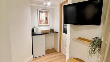 Een functionele keuken met een koelkast, een spoelbak en een aanrecht. Een flatscreen televisie is aan de muur bevestigd boven een klein houten tafeltje.