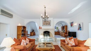A spacious living room with two sofas, a coffee table, and a fireplace. There are bookshelves, a TV, and artwork on the walls. - Casa Charador - Luxury Golf Villa (Alvor)