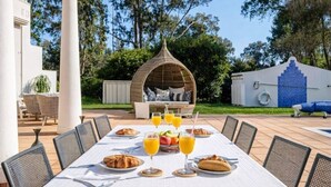 An outdoor dining area with a table set for breakfast, surrounded by chairs, and a wicker gazebo in the background. - Casa Charador - Luxury Golf Villa (Alvor)