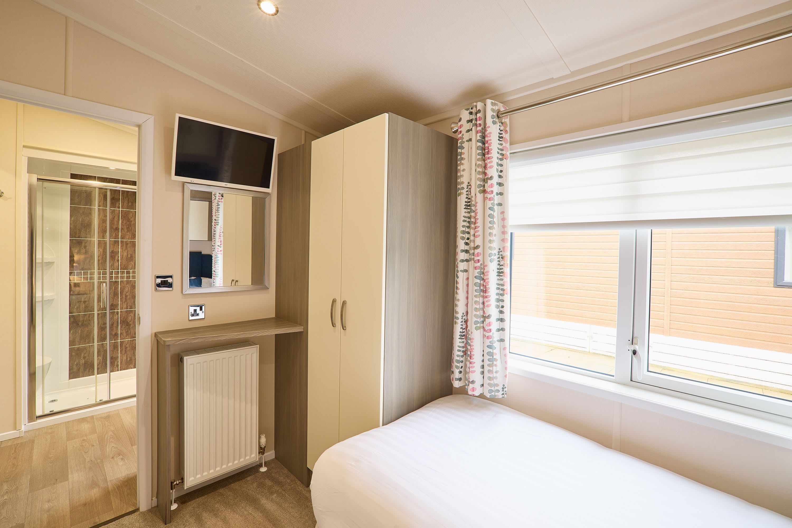 Een slaapkamer met een bed, een kledingkast, een spiegel, een radiator en een raam met gordijnen.