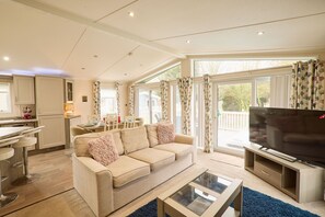 A modern living room with a sofa, coffee table, and TV. There is a kitchen area with bar stools and a dining table. - Host Stay Crucible Lodge (York)