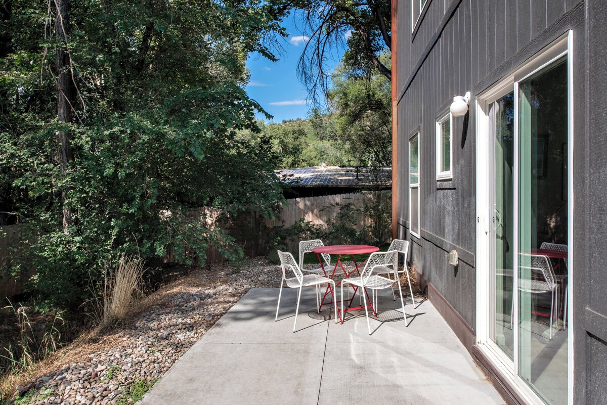 Une terrasse avec une table et des chaises, entourée d’un jardin et d’un bâtiment doté de grandes fenêtres.