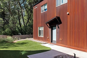A modern two-story building with a wooden exterior, a well-maintained lawn, and a clear sky.