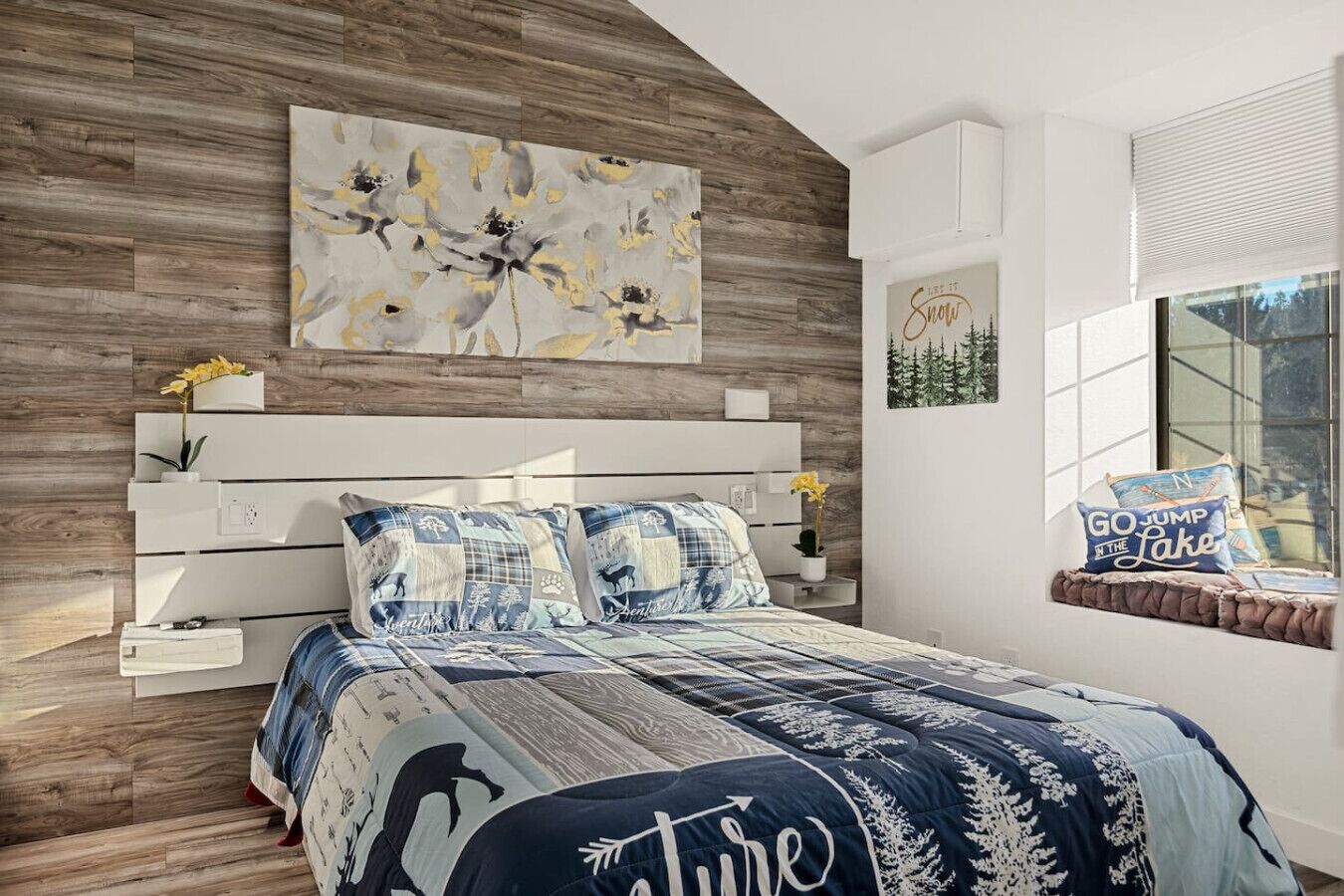 A modern bedroom with a wooden headboard, a large abstract painting, and a window with a view of trees.