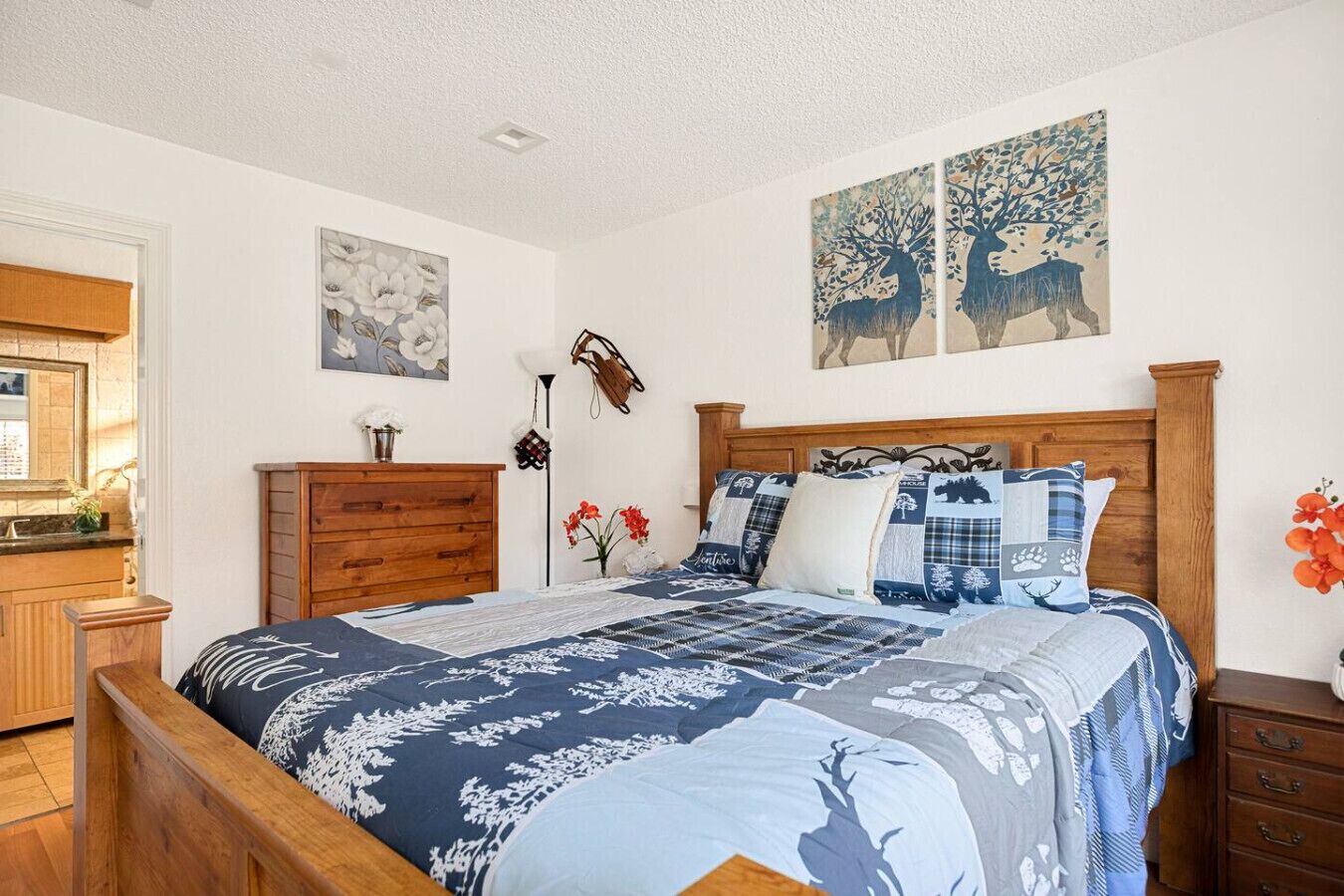 Een slaapkamer met een houten bed, een dressoir, een spiegel en twee aan de muur hangende schilderijen.