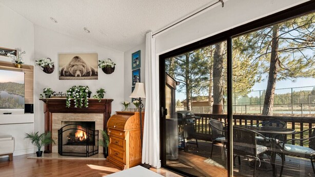 A modern living room with a fireplace, a dining area with outdoor seating, and a large sliding glass door leading to a deck. - Cozy 3BR Knotty Pine, Near Lake & Trails w Deck (Big Bear Lake)