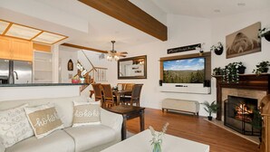 A cozy living room with a sofa, coffee table, fireplace, TV, and a dining area with chairs and a table. - Cozy 3BR Knotty Pine, Near Lake & Trails w Deck (Big Bear Lake)