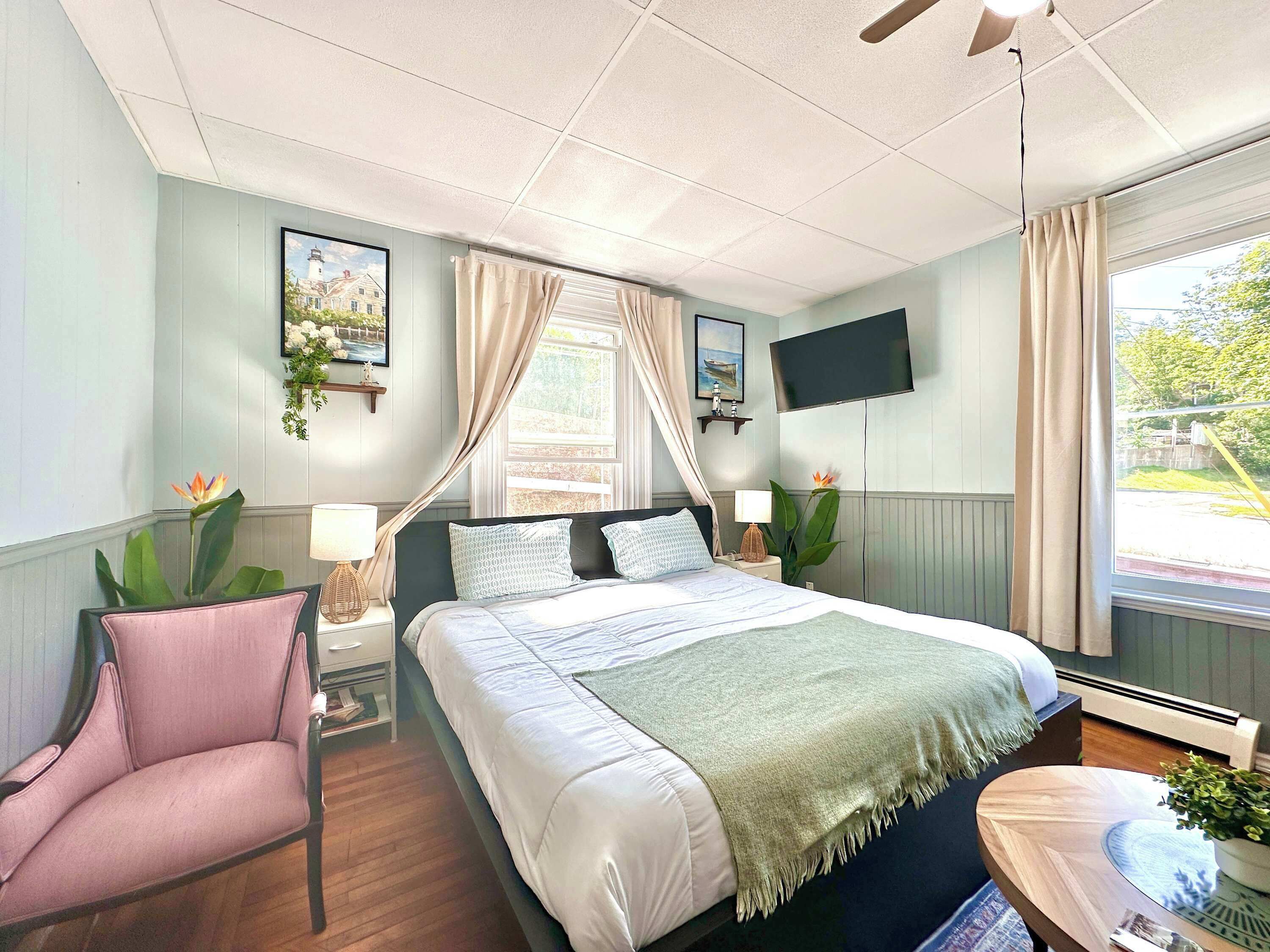 Ein Schlafzimmer mit einem Bett, einem Sessel, einem Nachttisch, einem Fernseher und einem Fenster.