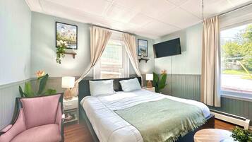 Ein Schlafzimmer mit einem Bett, einem Sessel, einem Nachttisch, einem Fernseher und einem Fenster.