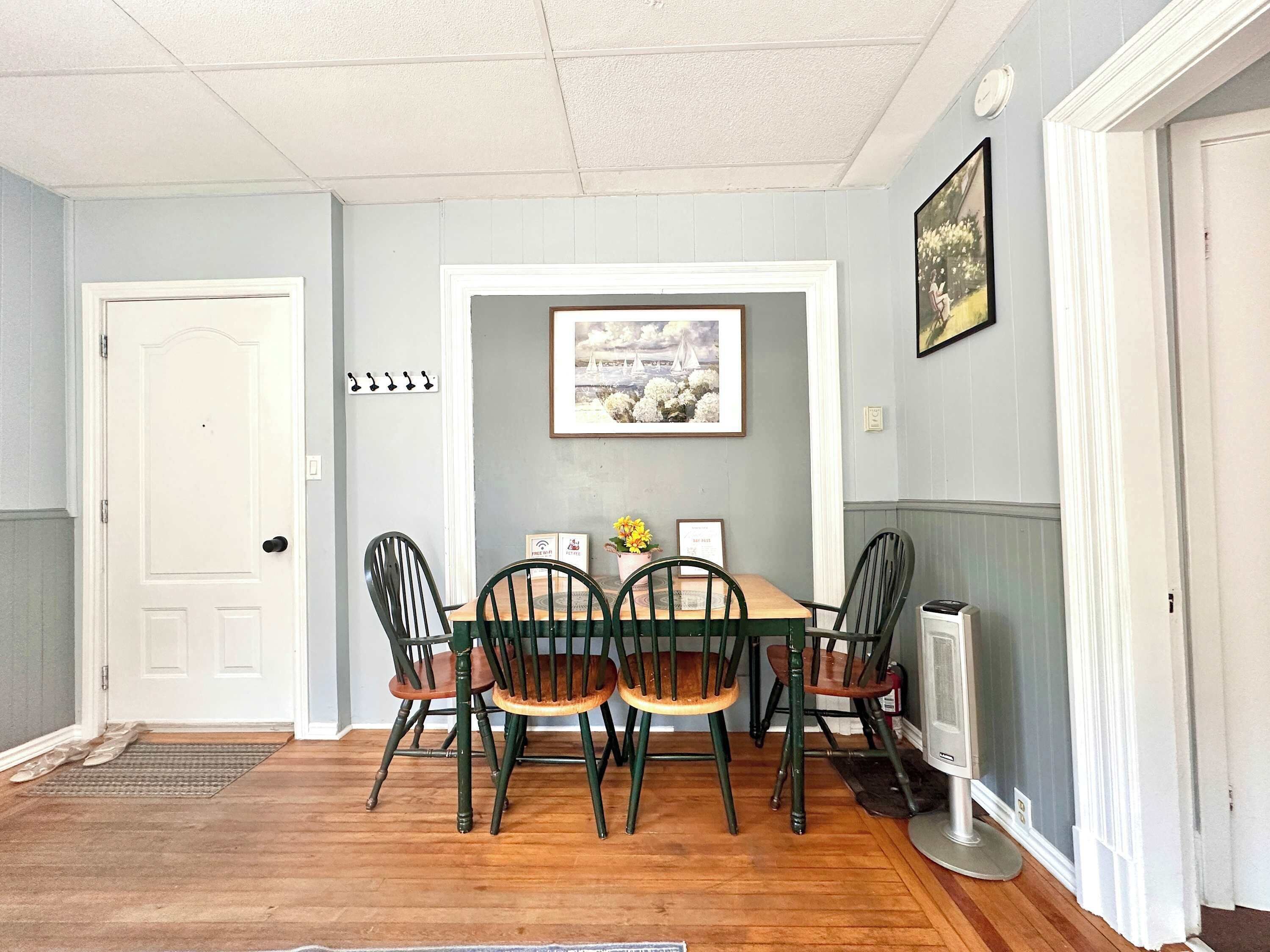 A dining area with a wooden table and chairs, a framed picture on the wall, and a door.