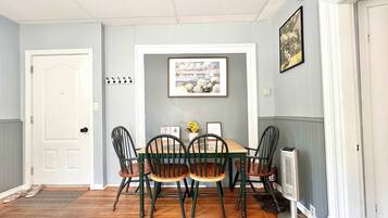 A dining area with a wooden table and chairs, a framed picture on the wall, and a door.