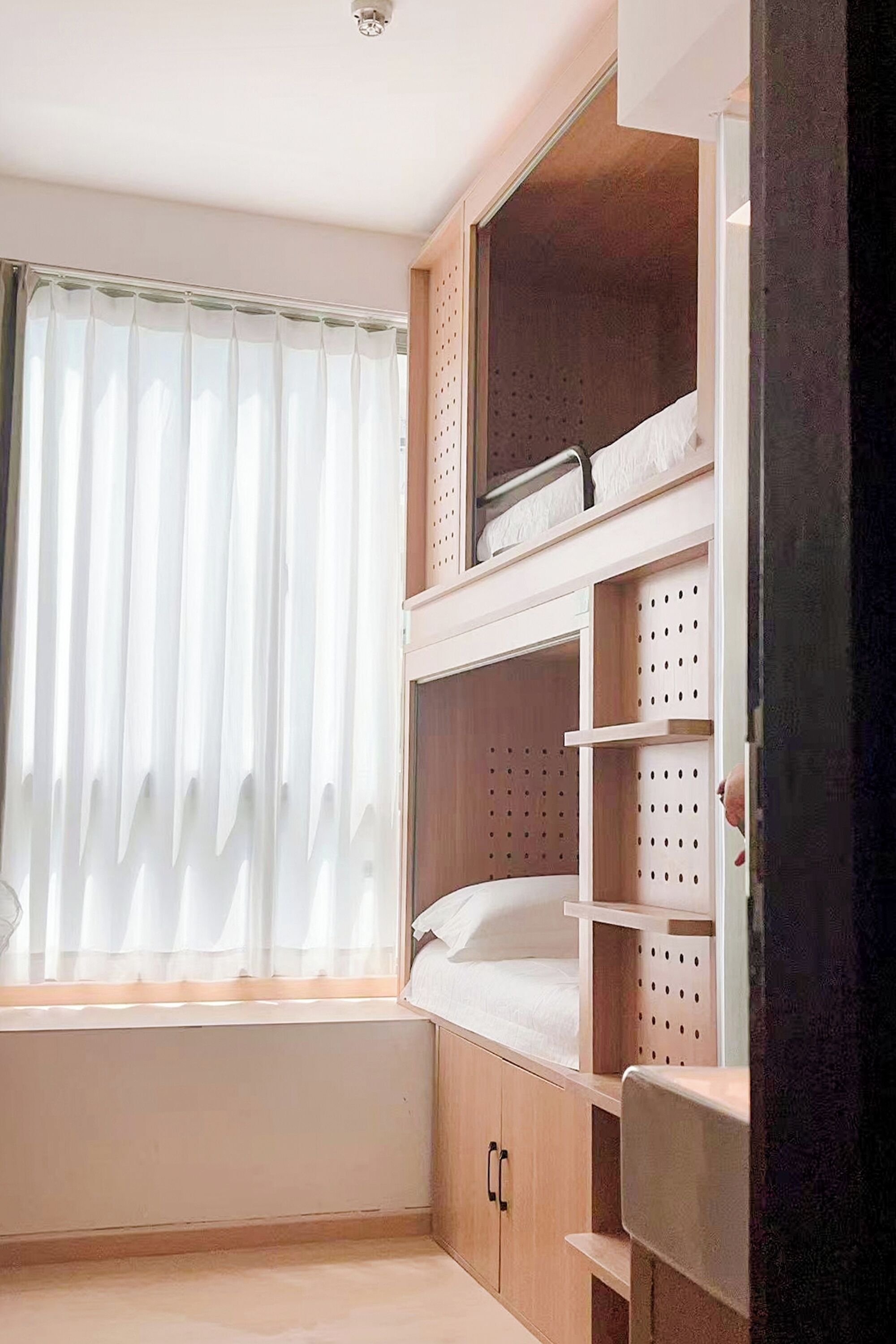 Una habitación con ventana, una cama litera y estantes empotrados.