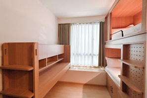Una habitación pequeña con literas, estantes de madera y una ventana con cortinas.