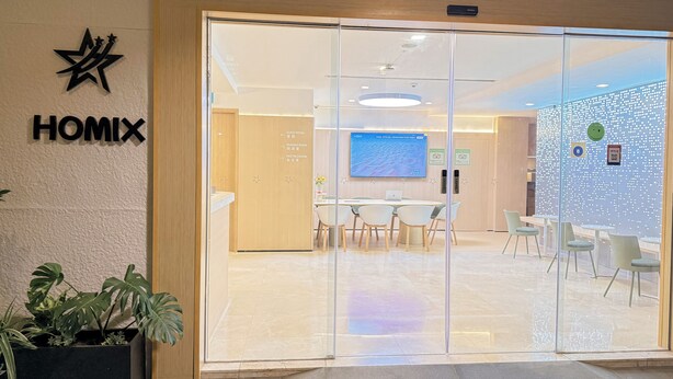 Zona de recepción de hotel con puerta de cristal, pantalla digital y señalización que indica habitaciones de huéspedes.