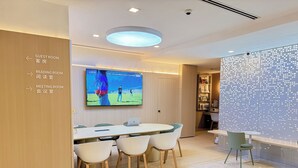Una sala de reuniones moderna con una gran televisión de pantalla plana, una mesa redonda con sillas y señales indicativas para huéspedes y salas de reuniones.