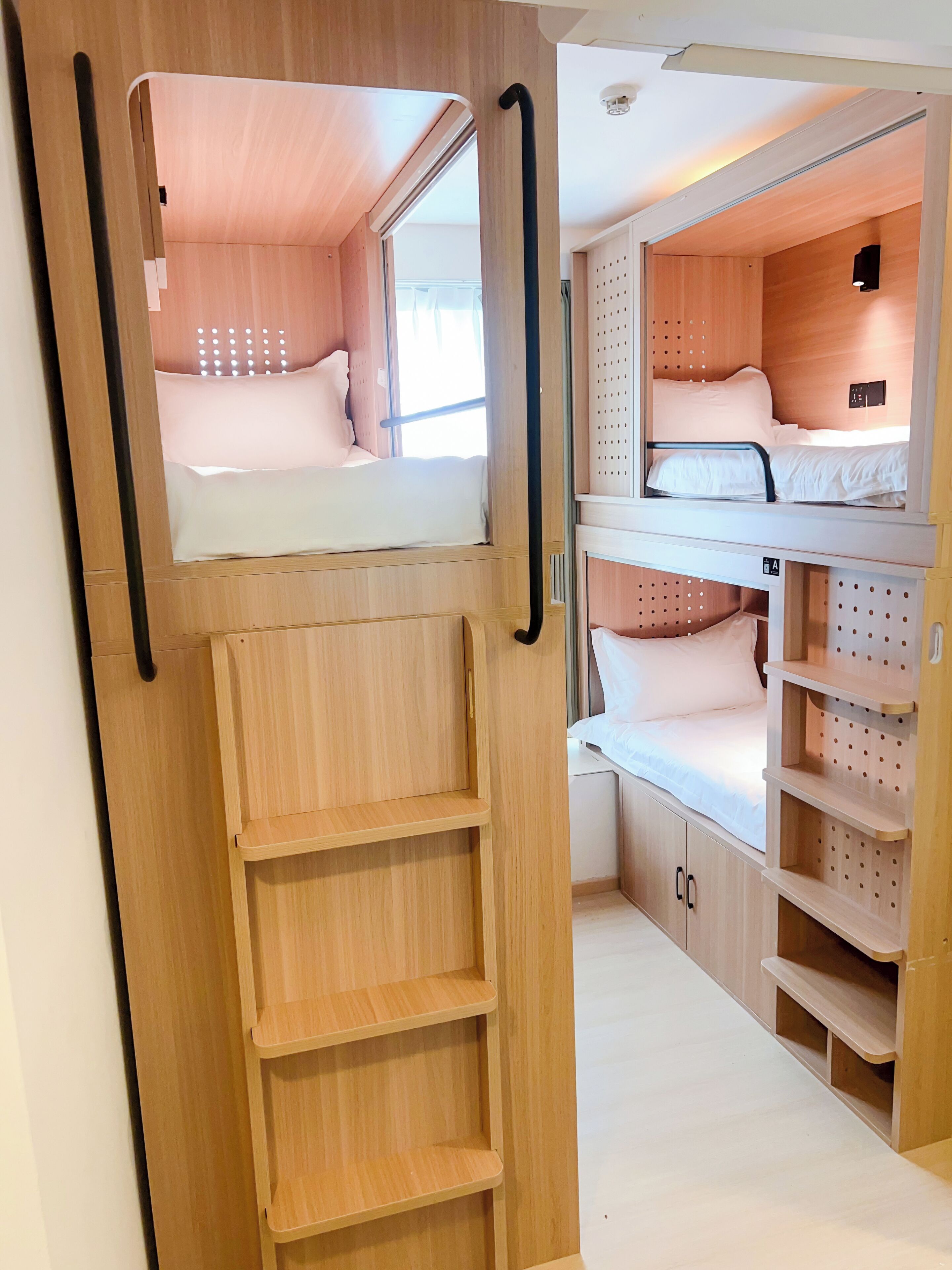 A compact, multi-level sleeping area with bunk beds and built-in shelves, featuring a wooden finish and a small window for natural light.