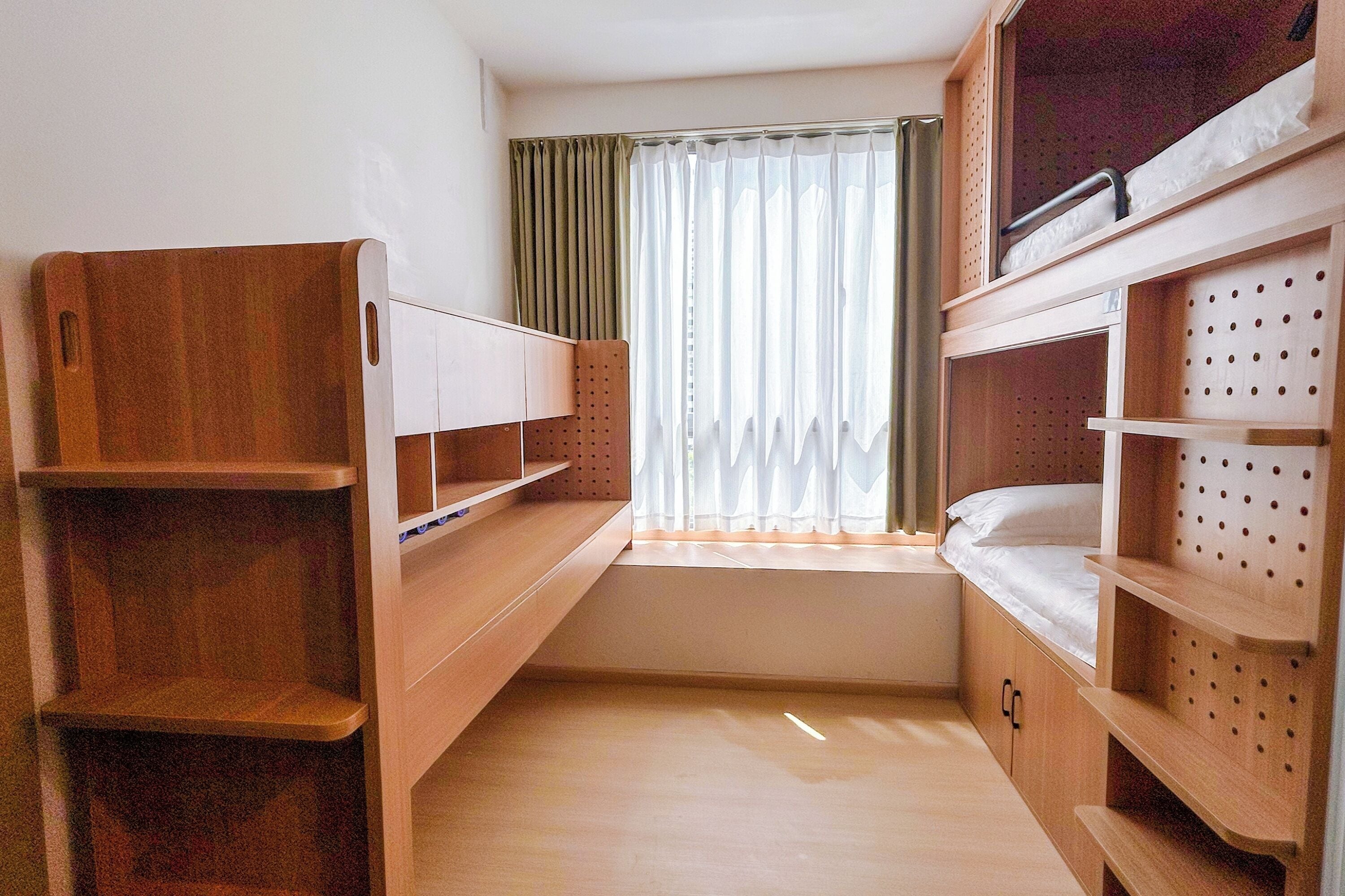 A compact room with two bunk beds, a window with curtains, and wooden shelves.