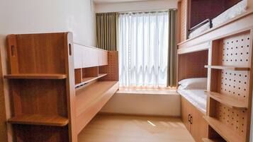 A compact room with two bunk beds, a window with curtains, and wooden shelves.