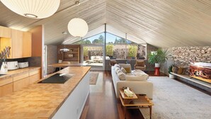 Un loft moderne comprenant une cuisine, un coin repas et un salon. Il est doté d’une grande verrière, d’un plafond en bois et d’un mur en pierre.