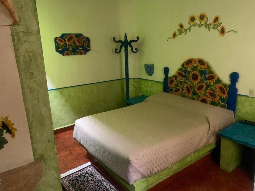 A bedroom with a bed, a nightstand, a wall-mounted coat rack, and a decorative sunflower mural.