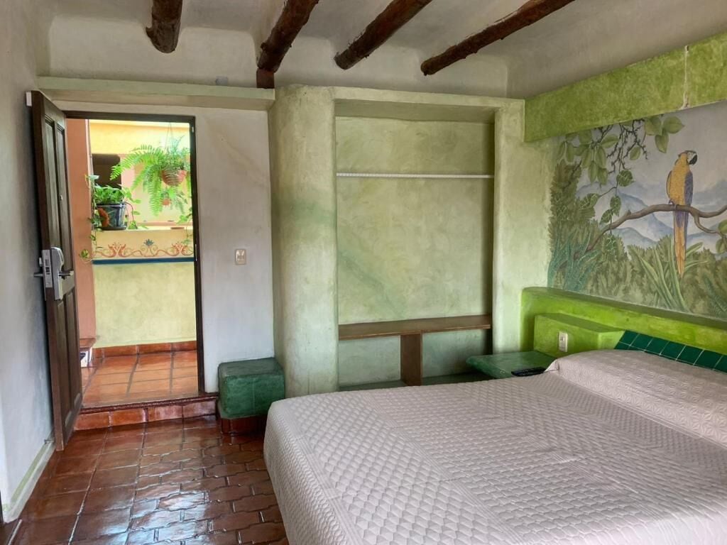 A bedroom with a bed, a green bench, a door leading to a balcony, and a mural of a bird on the wall.