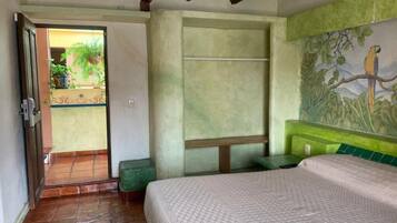 A bedroom with a bed, a green bench, a door leading to a balcony, and a mural of a bird on the wall.