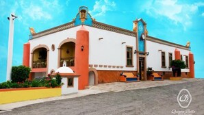 A two-story building with a white facade and orange accents, featuring a bell tower and arched windows.