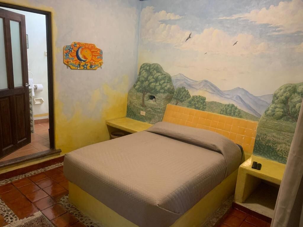 A bedroom with a bed, a nightstand, a wall mural, and a door.