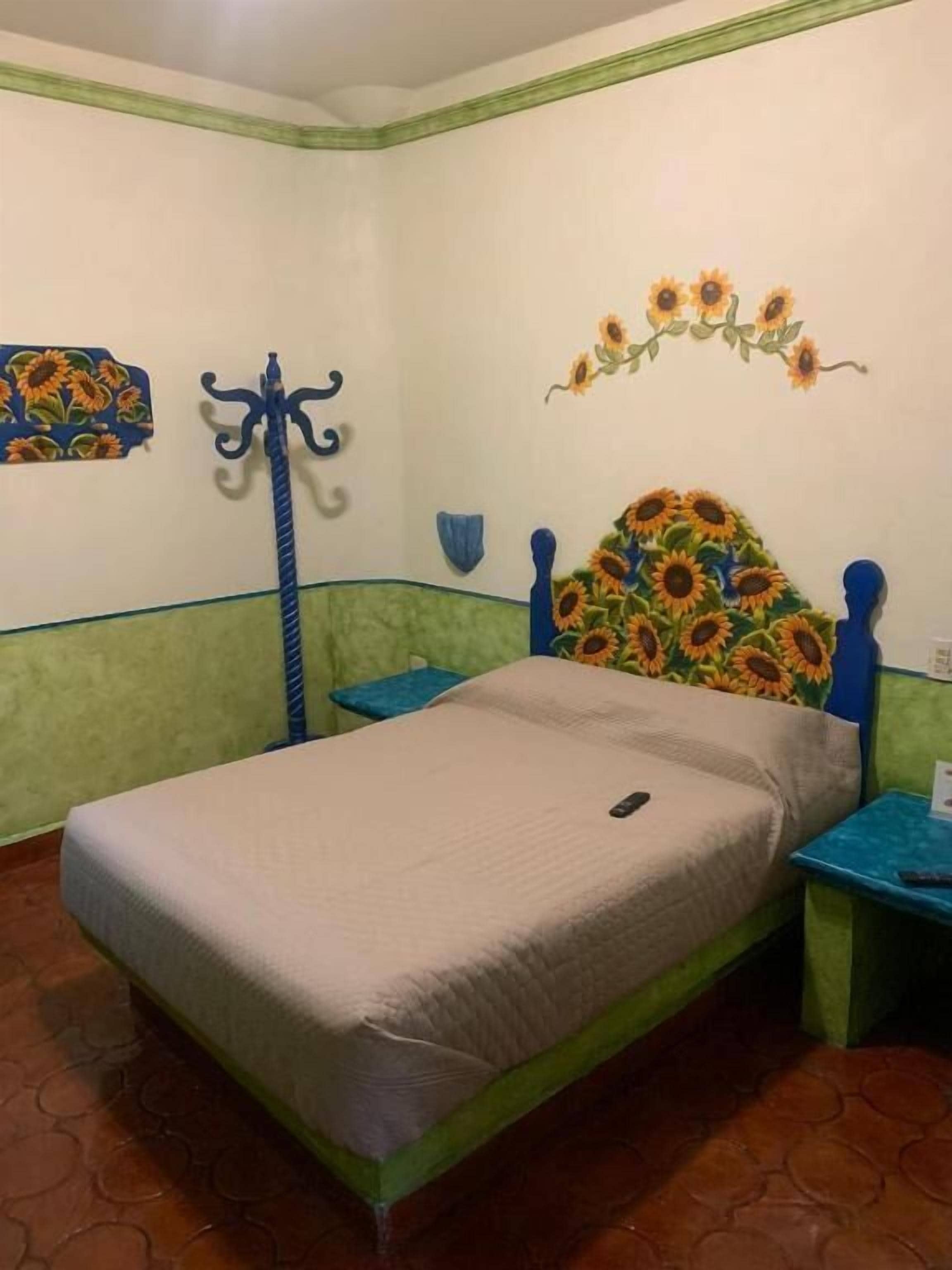 A single bed with a floral headboard, a blue coat rack, and a wall decoration of sunflowers.