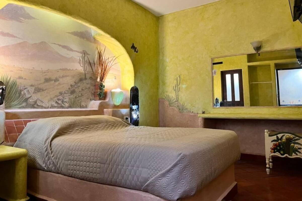 Une pièce comprenant un lit, une petite table, une chaise, un miroir et une fresque murale.
