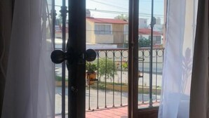 A room with a sliding glass door leading to a balcony. The balcony has a metal railing and a view of the street and buildings outside.