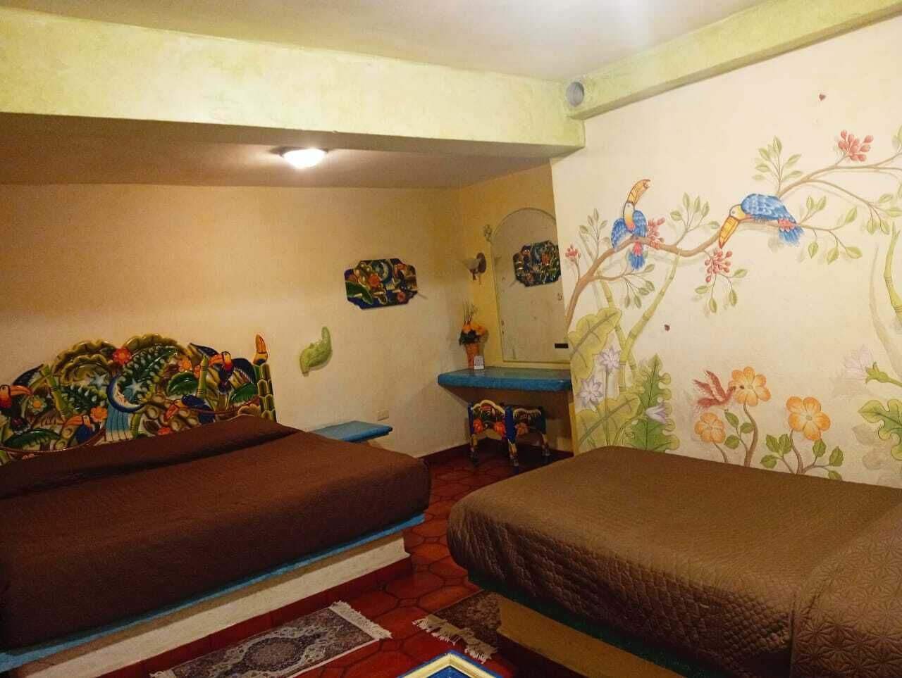 A room with two beds, a small table, a mirror, and a wall with a floral mural.