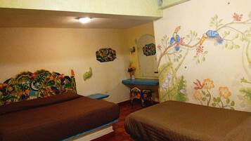 Una habitación con dos camas, una mesita, un espejo y un mural floral en la pared.