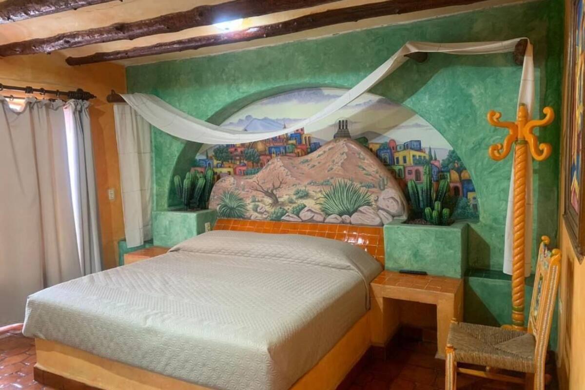 Une pièce comprenant un lit, une chaise, une fresque murale et une décoration en forme d’épée.