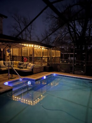 Piscina con hidromasaje y zona de estar en la terraza, rodeada por un porche cubierto con luces colgantes.
