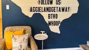 A room with a blue wall, a decorative wall sign, a patterned sofa, and a small round table. - Tournament Ready Stay •Close to Parks •3 bedroom/2 bath •Pool/HotTub (College Station)