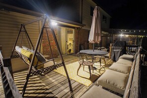 Un patio techado al aire libre con una silla colgante, una mesa con sillas y asientos acolchados.