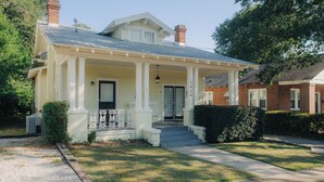 Una casa de dos pisos con un porche, una chimenea y el número 1829 en la fachada.