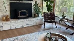 Una sala de estar con chimenea de ladrillo, televisor de pantalla plana y un ventanal con vistas a árboles.