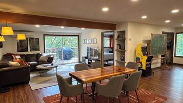 Un salon moderne avec une table à manger en bois, des chaises grises, un canapé et un téléviseur.
