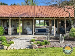 A covered outdoor seating area with a rustic wooden structure, a bar, and a garden with rocks and plants.