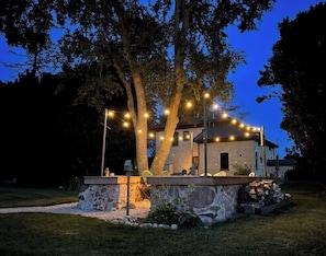 A stone patio with outdoor seating, a tree, and string lights.
