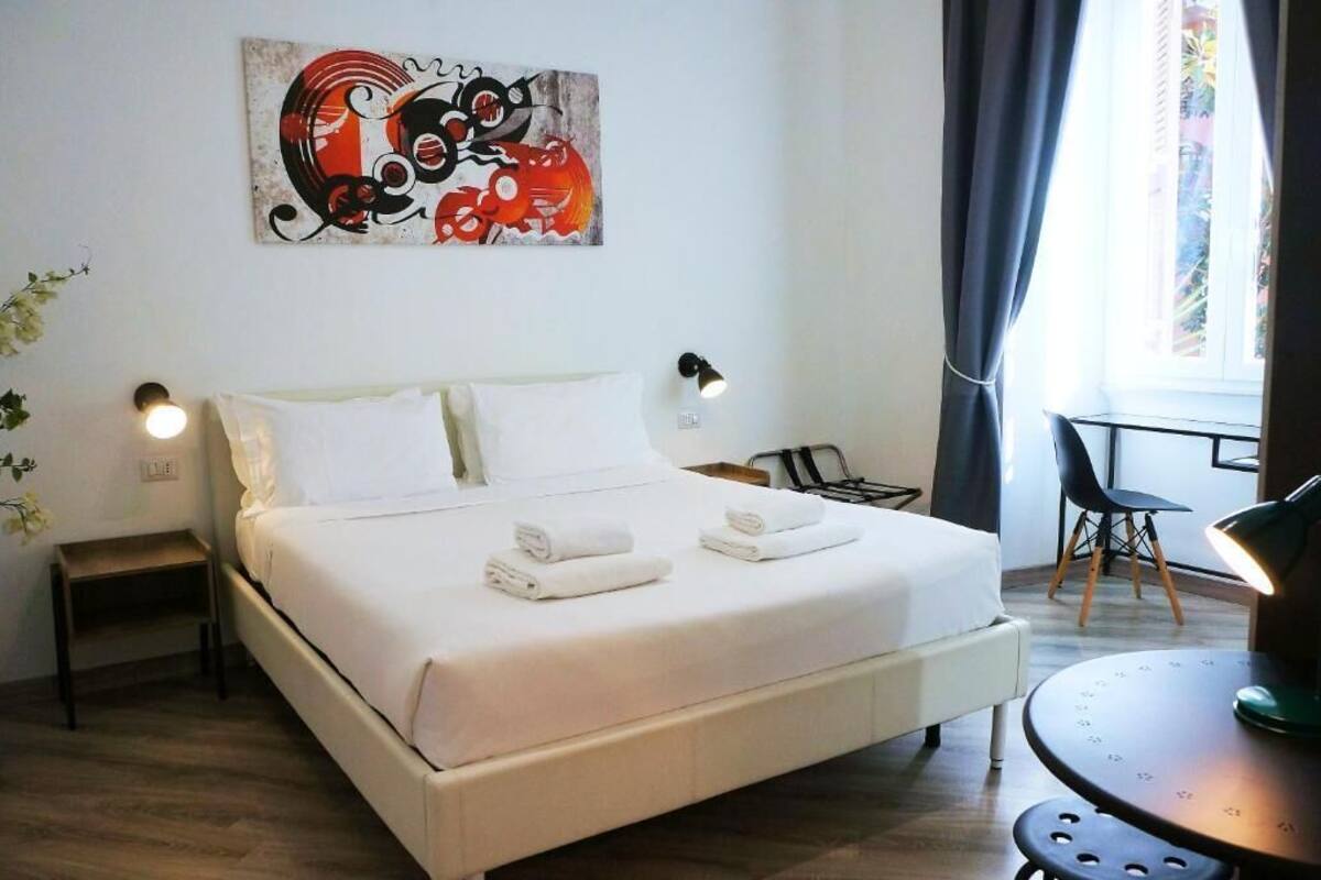 Ein Hotelzimmer mit einem großen Bett, zwei Nachttischlampen, einem kleinen Tisch und einem Fenster mit Vorhängen.