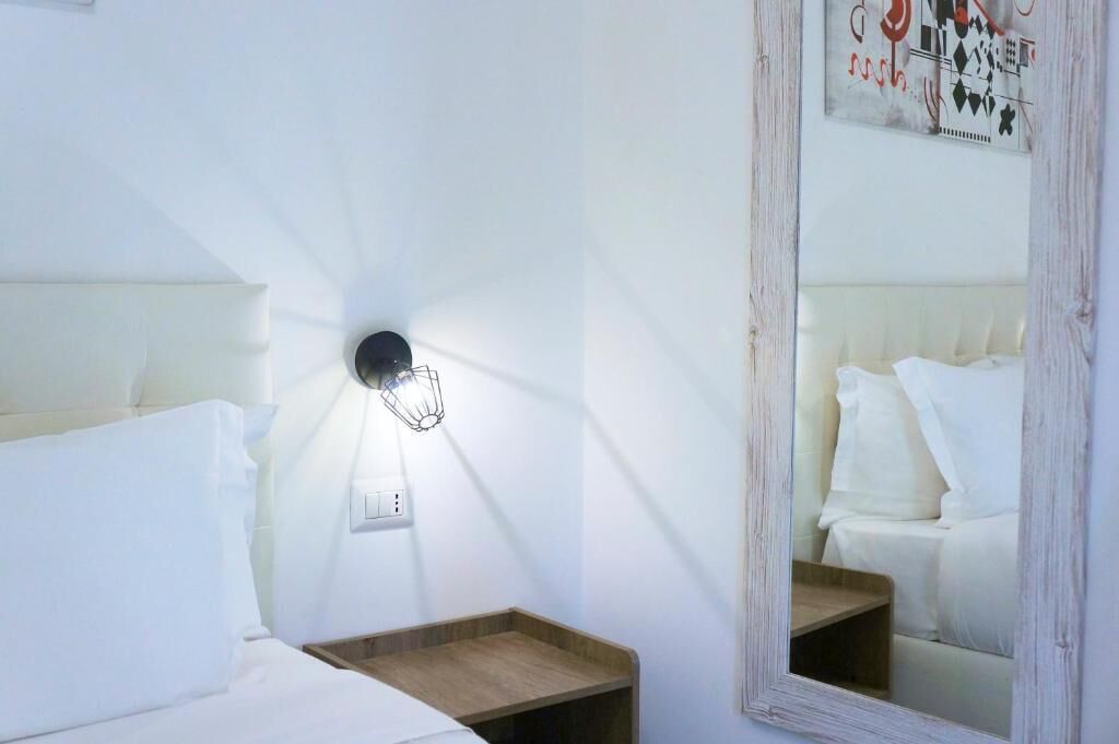 A hotel room with a bed, bedside tables, a wall-mounted light fixture, and a mirror.