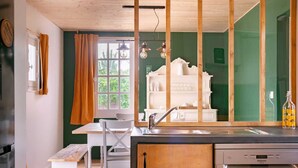 Een keuken met een houten kookeiland, een spoelbak en een vaatwasser. Er is een raam met gordijnen, een witte stoel en een bankje.