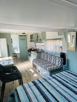 Interior compacto de una autocaravana con kitchenette, cama y zona de comedor.